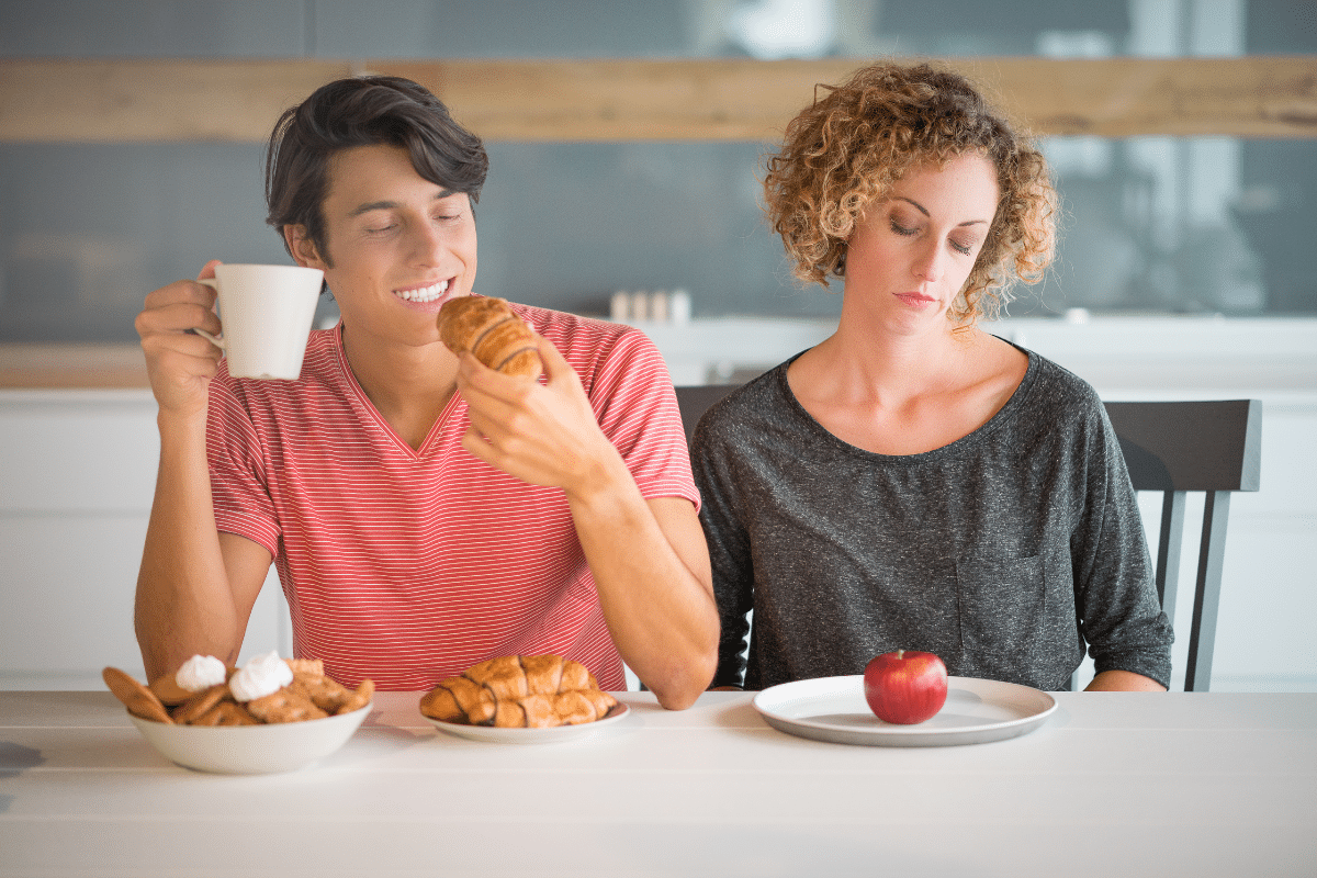 having to miss out diet pic man eating lots of pasries whilst a woman has a plate with an apple on it. she doesn't look happy